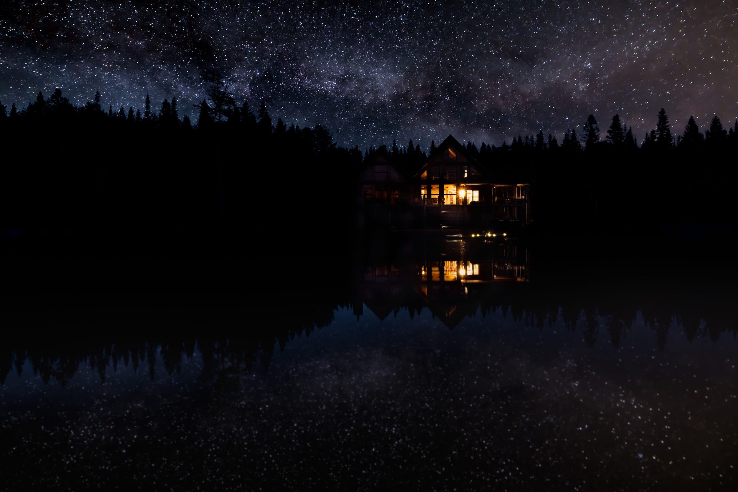 A timber lodge glowing warm across a still lake beneath the Milky Way