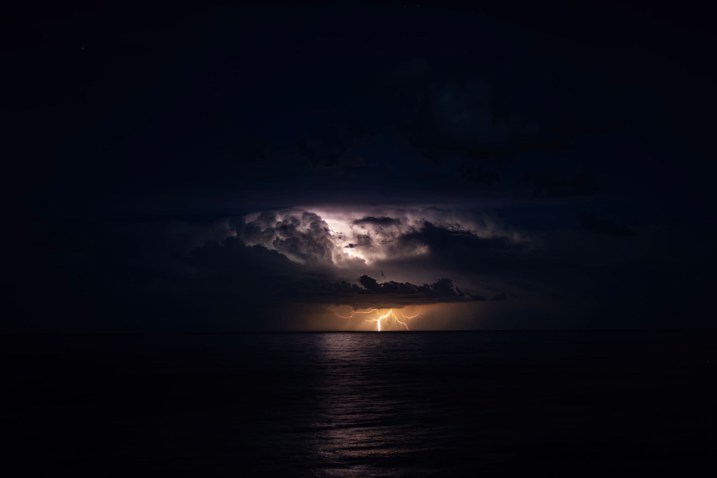 A distant storm cell with lightning glowing gold over dark water